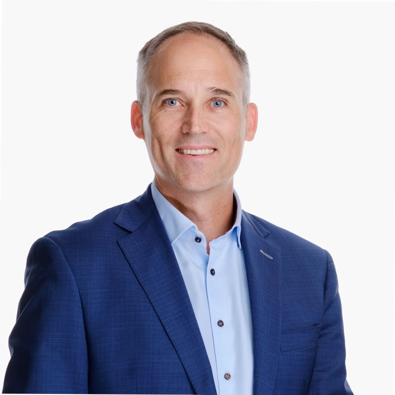 Smiling man in a blue suit and light blue shirt against a white background (professional headshot)