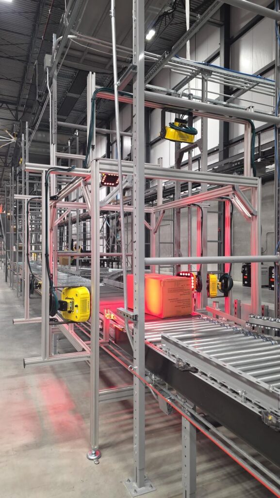 Industrial packaging line with metal framework, conveyors, and a cardboard box moving along the belt.